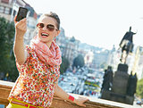 Smiling young woman taking selfie with digital camera in Prague