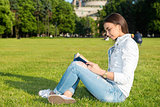 Girl-student sit on lawn and reads textbook.