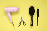 Hair dryer, brush, comb and scissors on yellow paper background