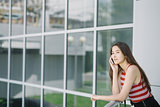 Young Asian woman talking on smartphone near glass wall