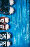 Three pairs of old sneakers on blue worn wooden background