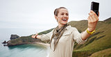 woman hiker taking selfie in front of ocean view landscape