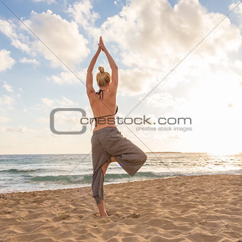 Woman practicing yoga on sea beach at sunset.