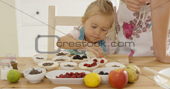 Little girl placing berries on muffins