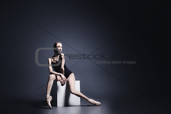 Young ballerina in a black suit is dancing in dark studio