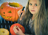 Beautiful girl with green eyes cut a pumpkin for Halloween.