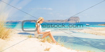 Woman reading book, enjoying sun on beach.