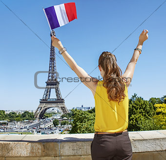 young woman rising French flag in front of Eiffel tower in Paris