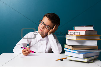 Pensive cute boy with glasses sitting at a table