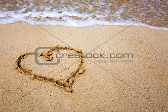 Heart symbol on the sand and sea wave.