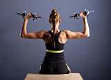 Fit young woman doing shoulder raises with dumbbells, isolated ongray background.