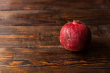 One red and ripe pomegranate lying on the dark wooden table
