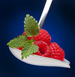 Raspberries on spoon with mint leaves on blue background