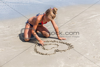 Love the sea - little girl drawing heart shape in the sand