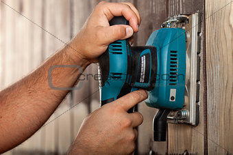 Male hands using a vibrating sander on wooden surface