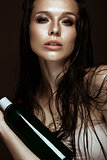 Beautiful girl with a bright make-up, wet hair and skin, bottle of cosmetic products in hands. Beauty face.