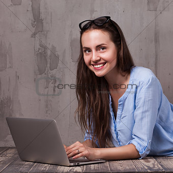Young smiling woman lying on the wooden floor with laptop