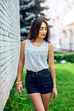 Girl brunette in summer in the park with resting in shorts and white blouse on background fashion lifestyle, gentle look. Sensual make-up, tanned skin bright red lipstick. Portrait of woman.