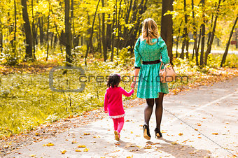 Mother and daughter walking in autumn park, back view