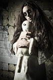 Horror style shot: strange sad girl with moppet doll in hands