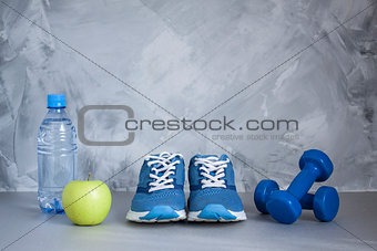 Sport shoes, dumbbells, apple, bottle of water on gray concrete 