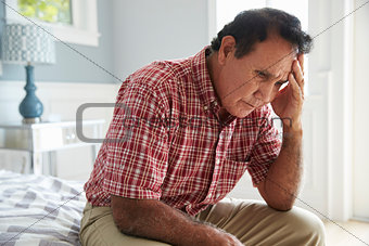 Senior Hispanic Man Sitting On Bed Suffering With Depression