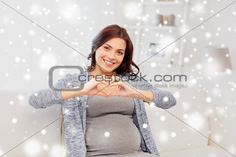 happy pregnant woman making heart gesture at home