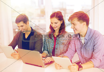 three smiling students with laptop and tablet pc