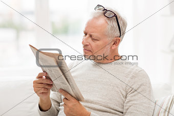 senior man in glasses reading newspaper at home