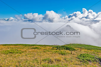 Clouds cover mountain tops at autumn day time.