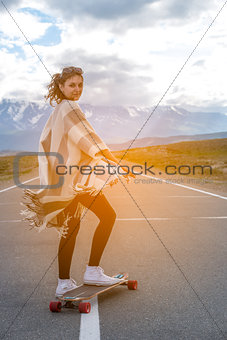 Young cute girl rides skateboard on road in the mountains
