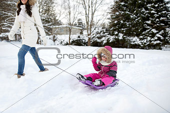 happy mother pulling sled with child in winter