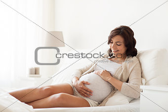 happy pregnant woman lying on bed at home