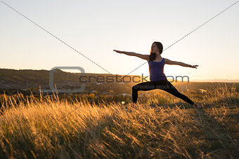 Woman doing yoga warrior II pose during sunset