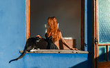 Beautiful girl with red hair and cat at the window