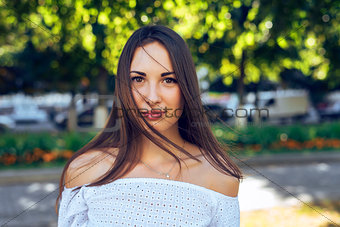 Close-up portrait of beautiful brunette girl, standing in the park, summer, white blouse, long hair, sensual look, the concept  student, fashion lifestyle, rest in a  .