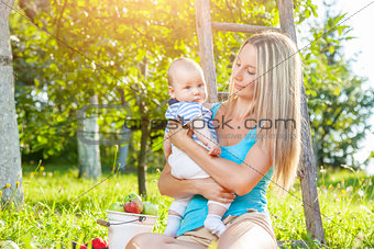 Beautiful mother with baby sitting outdoors on a blanket
