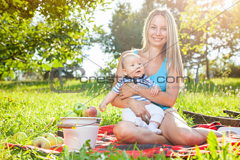 Beautiful mother with baby sitting outdoors on a blanket