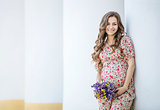Pretty pregnant woman with a bunch of flowers near the column
