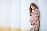 Happy pregnant woman leaning against the column on summer day