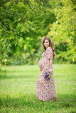 Beautiful pregnant woman carrying flowers outdoors in summer park