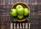 Green organic healthy apples in bowl on wooden board