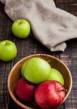 Green and red organic  apples in bowl on wooden board