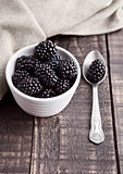 Blackberry in white bowl and spoon on grunge wooden board