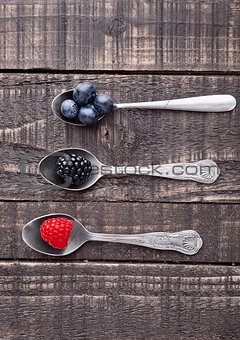 Raspberry blueberry and blackberry on spoon and wooden table
