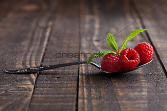 Raspberries on old spoon and mint on grunge wooden board