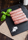 Raw beef sausages with salt and basil on stone board