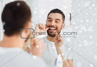 man with dental floss cleaning teeth at bathroom