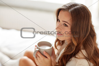happy woman with cup of cocoa in bed at home