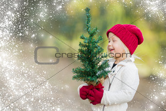 Baby Girl In Mittens Holding Small Christmas Tree with Snow Effe
